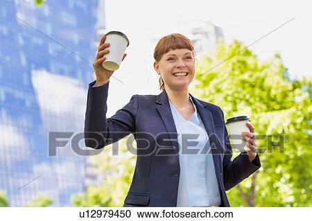 Stock Image - Young beautiful businesswoman holding two cups of coffee. Fotosearch