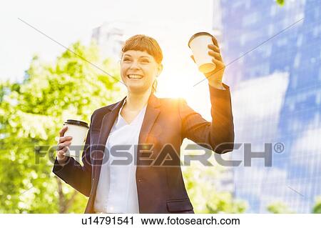 Stock Image - Young beautiful businesswoman holding two cups of coffee. Fotosearch