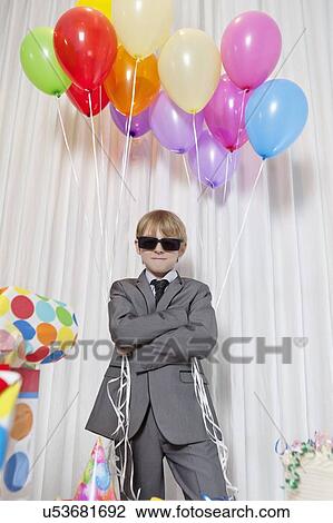 Young boy wearing sunglasses and standing with arms crossed holding party balloons View Large Photo Image Stock Image - Young boy wearing sunglasses and standing with arms crossed holding party balloons. Fotosearch