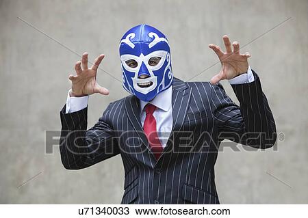 Stock Image - Young businessman gesturing in wrestling mask and pinstripes suit over gray background. Fotosearch