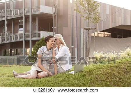 Young businesswoman whispering to female colleague on office lawn View Large Photo Image Stock Photo - Young businesswoman whispering to female colleague on office lawn. Fotosearch