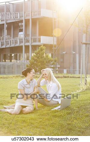 Stock Image - Young businesswomen gossiping in office lawn. Fotosearch