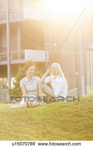 Stock Photo - Young businesswomen gossiping in office lawn. Fotosearch