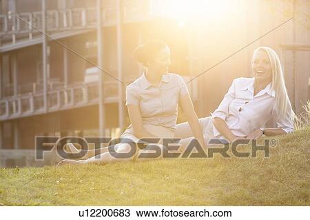 Stock Image - Young businesswomen relaxing on office lawn. Fotosearch