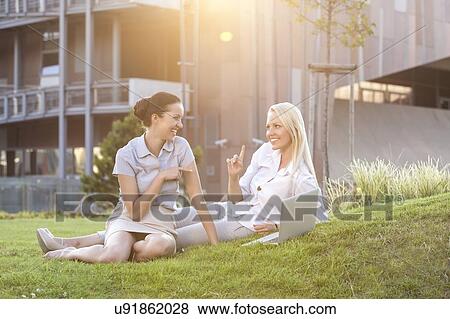Stock Photo - Young businesswomen spending leisure time on office lawn. Fotosearch
