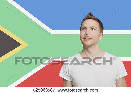 Stock Photo - Young Caucasian man in white t-shirt day dreaming against South African flag. Fotosearch