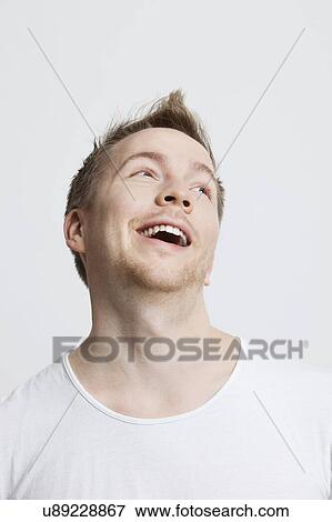 Stock Photo - Young Caucasian man in white t-shirt day dreaming against white background. Fotosearch