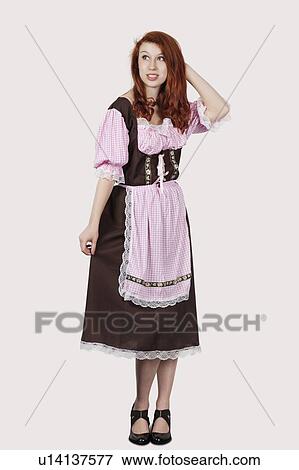 Stock Photo - Young confused woman in maid costume standing against gray background. Fotosearch