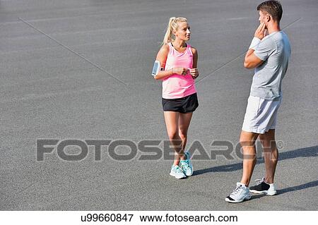 Stock Photo - Young couple standing while talking after exercising. Fotosearch