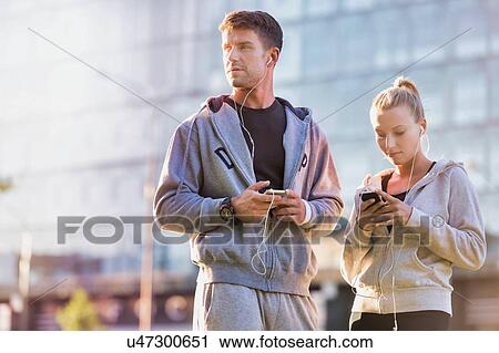 Stock Image - Young couple standing while using smartphone after working out. Fotosearch