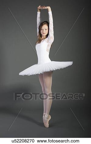 Stock Image - Young female ballet dancer posing over grey background. Fotosearch