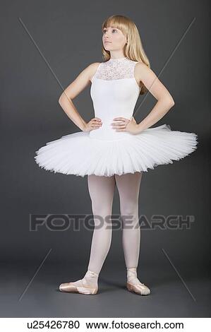 Stock Image - Young female ballet dancer with hands on hips standing over grey background. Fotosearch