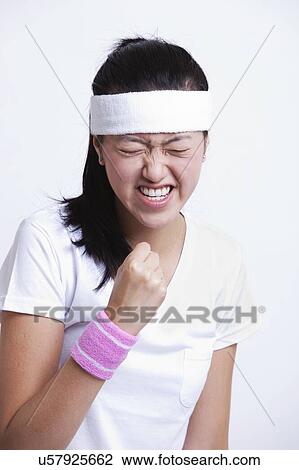 Stock Image - Young female tennis player celebrating success against white background. Fotosearch
