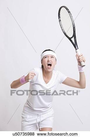 Stock Photo - Young female tennis player with racket cheering against white background. Fotosearch