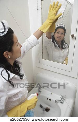 Young housemaid cleaning mirror above wash basin View Large Photo Image Stock Photograph - Young housemaid cleaning mirror above wash basin. Fotosearch