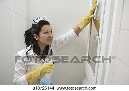 Picture - Young maidservant cleaning mirror. Fotosearch