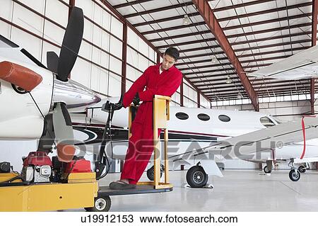Stock Image - Young male aviation mechanic repairing airplane in airplane hangar. Fotosearch