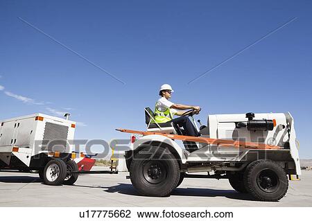 Stock Image - Young male ground crew driving truck at airport runway. Fotosearch