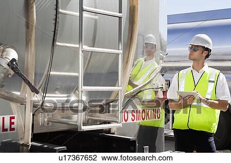 Stock Image - Young male worker using tablet PC as he inspects oil tanker. Fotosearch