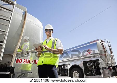 Young male worker using tablet PC as he inspects oil tanker View Large Photo Image Stock Photograph - Young male worker using tablet PC as he inspects oil tanker. Fotosearch