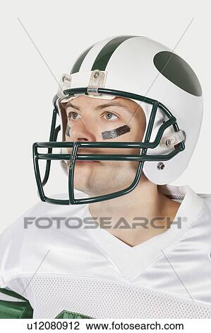 Young man in football uniform looking away against gray background View Large Photo Image Stock Image - Young man in football uniform looking away against gray background. Fotosearch
