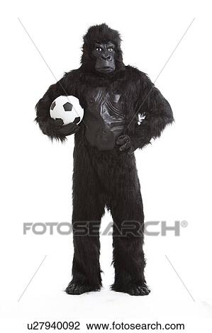 Stock Image - Young man in gorilla costume holding soccer ball against white background. Fotosearch