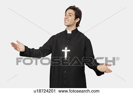 Stock Image - Young man in priest costume gesturing against gray background. Fotosearch