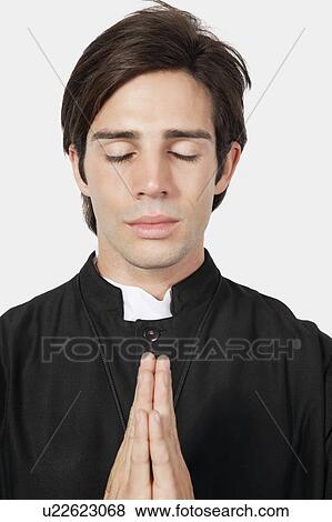 Stock Photo - Young man in priest costume praying against gray background. Fotosearch