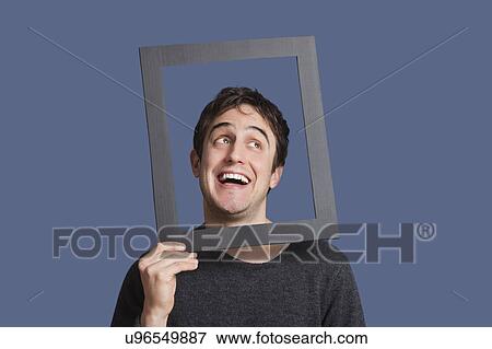 Young man laughing through frame over blue background View Large Photo Image Stock Photo - Young man laughing through frame over blue background. Fotosearch