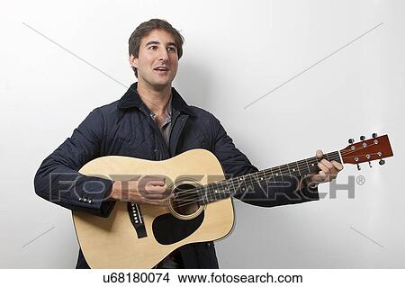 Picture - Young man playing guitar while signing against white background. Fotosearch