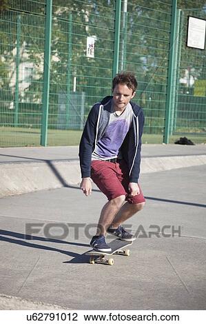 Stock Image - Young man skateboarding on road. Fotosearch