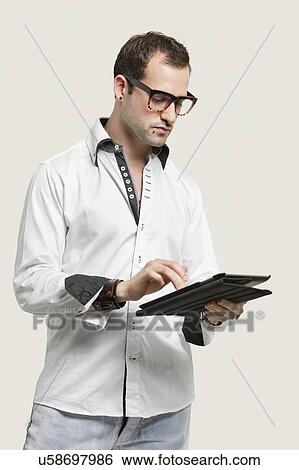 Young man using digital tablet against gray background View Large Photo Image Stock Photograph - Young man using digital tablet against gray background. Fotosearch