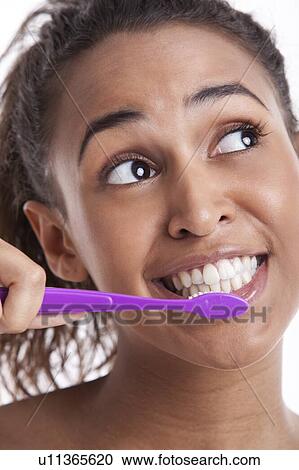 Stock Image - Young Mixed Race woman brushing teeth against white background. Fotosearch