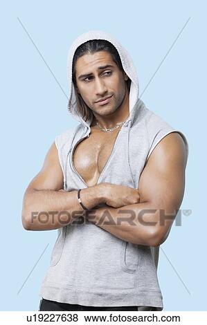 Young muscular man wearing hooded jacket standing with arms crossed against colored background View Large Photo Image Stock Photo - Young muscular man wearing hooded jacket standing with arms crossed against colored background. Fotosearch
