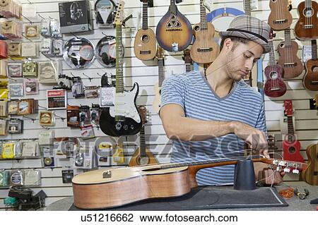 Stock Image - Young music store owner restringing guitar. Fotosearch