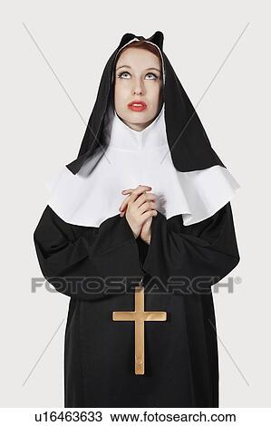 Stock Image - Young nun praying against gray background. Fotosearch