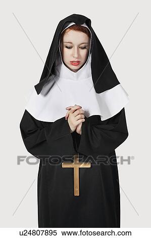 Stock Photography - Young nun with cross praying against gray background. Fotosearch
