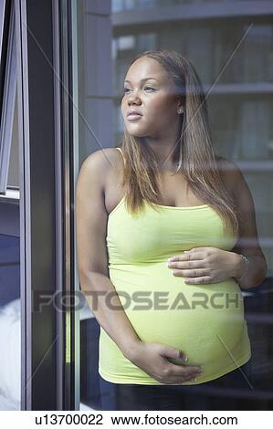 Stock Image - Young pregnant woman with hands on stomach looking away. Fotosearch
