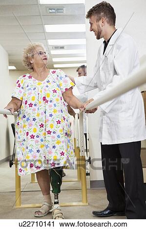 Stock Image - Young technician communicating with senior woman having ambulatory therapy. Fotosearch