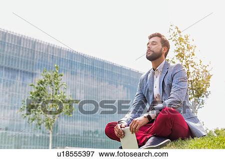 Young thoughtful businessman sitting on the grass while holding digital tablet View Large Photo Image Stock Photo - Young thoughtful businessman sitting on the grass while holding digital tablet. Fotosearch