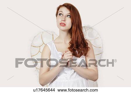 Picture - Young woman dressed as an angel looking away against gray background. Fotosearch