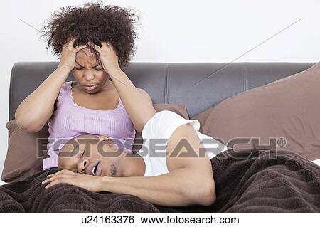 Stock Photograph - Young woman having headache while man sleeping on her lap in bed. Fotosearch