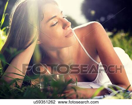 Stock Image - Young woman lying in meadow, leaning on elbow. Fotosearch