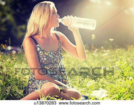 Young woman sitting in meadow drinking water from bottle View Large Photo Image Stock Image - Young woman sitting in meadow drinking water from bottle. Fotosearch