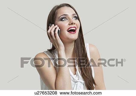 Stock Photo - Young woman using cell phone while looking up over gray background. Fotosearch