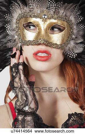 Young woman with feathered eye mask looking away against gray background View Large Photo Image Picture - Young woman with feathered eye mask looking away against gray background. Fotosearch