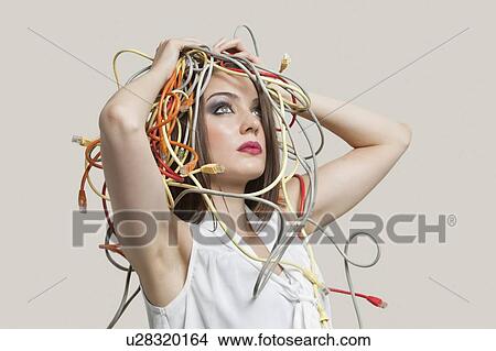 Picture - Young woman with head tangled in colorful cables over gray background. Fotosearch