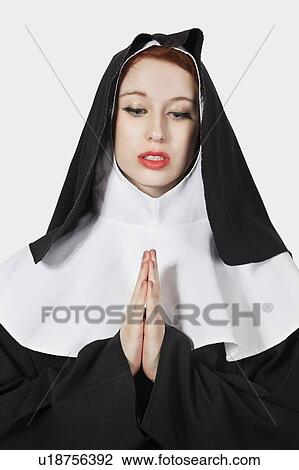 Stock Image - Young woman with in nun costume praying against gray background. Fotosearch