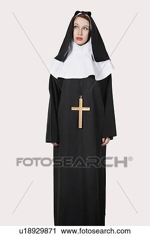 Stock Image - Young woman with in nun costume standing against gray background. Fotosearch