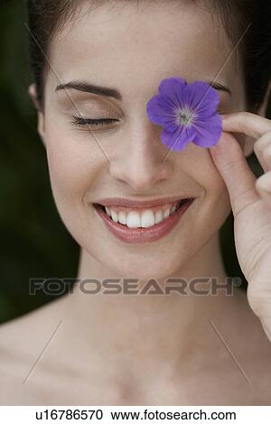 Stock Image - Young woman holding flower over her eye. Fotosearch